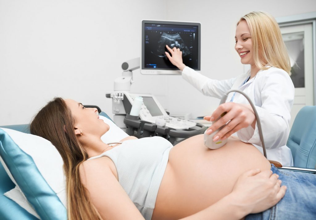 Doctor pointing at screen and showing baby to future mother